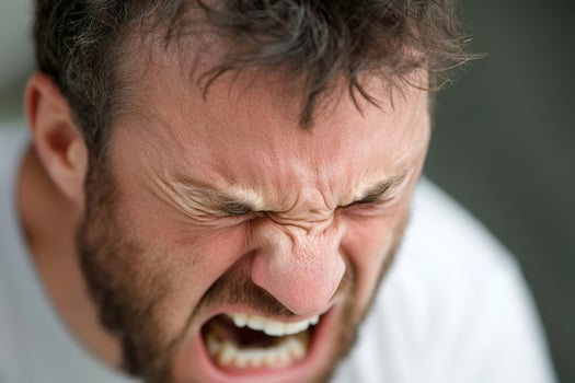 A man with a beard and a white shirt is making an angry face photo