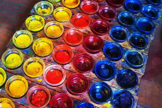 A neatly arranged set of glass pigment bowls displays a vivid range of primary colors yellow, red, and blue on a wooden tray. photo
