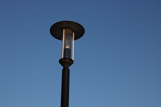 A beautiful iron streetlight with a round lid against a clear blue sky. A minimalist composition with classic design details photo