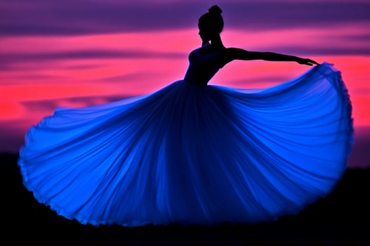 A woman in a blue dress is dancing in front of a sunset photo