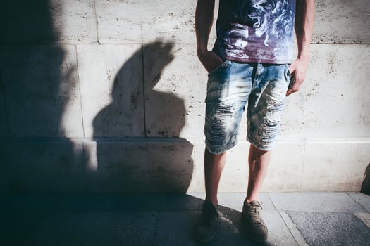 Casual Man Wearing Graphic T-shirt and Distressed Shorts Standing Against Stone Wall photo
