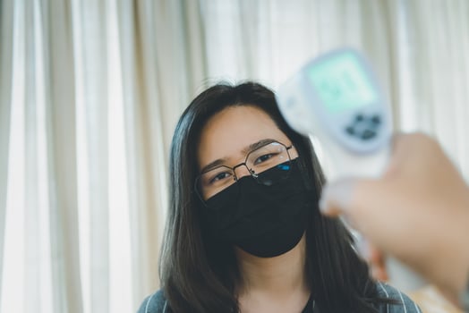 A woman wearing a face mask and holding a thermometer photo