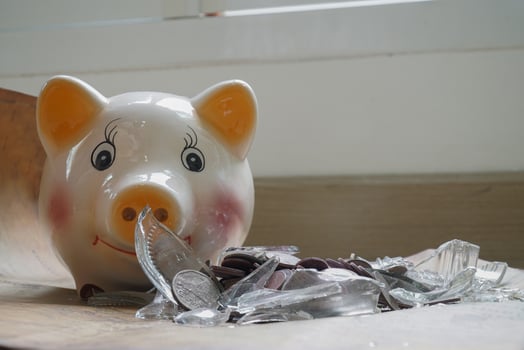 Broken piggy bank lies wooden surface, surrounded by scattered coins and shards of glass, symbolizing financial loss or savings disruption. scene is set against bright background, evoking sense photo