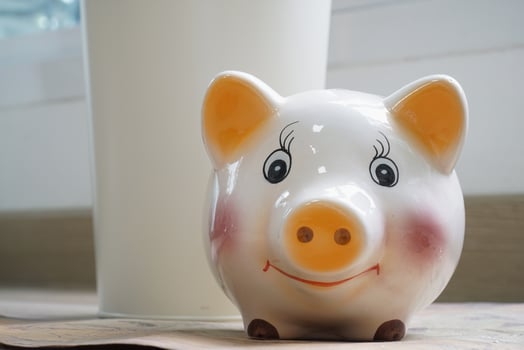 Cheerful ceramic piggy bank with smiling face sits on wooden surface, symbolizing savings and financial planning. background is softly blurred, highlighting piggy bank playful design photo