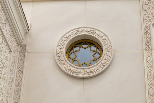 A round window with floral ornamentation and a carved frame on the white marble wall of the mosque photo