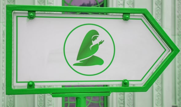 A sign indicating the place of prayer and depicting a Muslim woman, against the backdrop of a mosque wall photo