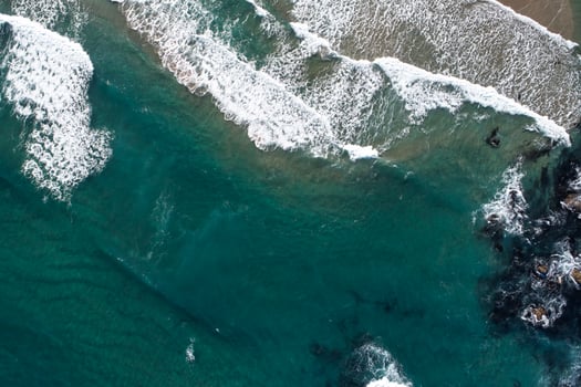 A Dynamic Seascape with Foamy Waves and a Rocky Beach, aerial top down drone view photo