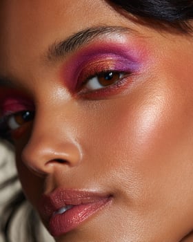 Detailed cheek macro of Indian model showing vibrant ombre blush in layered copper, magenta, and crimson hues with radiant skin finish and white blurry background photo