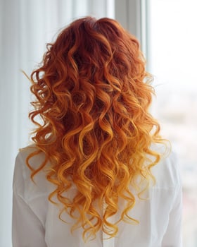 Fiery ombre curly hair seen from the back transitioning from intense fire red at the roots to neon orange mid lengths and sunshine yellow ends photo