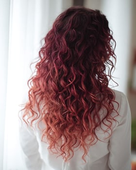 Back view of long curly hair with rich ombre transition from deep burgundy roots to cherry red midsection and soft coral colored tips photo
