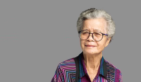 Beautiful senior woman with short white hair and glasses smiles at the camera while standing against a gray background. photo