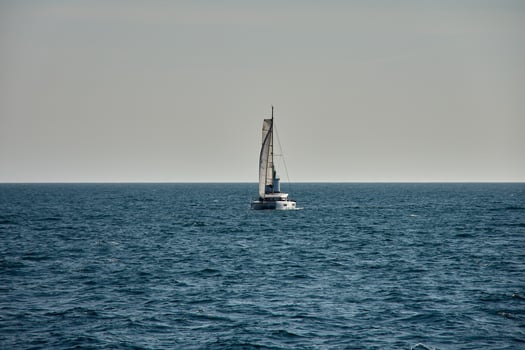A sailboat with a sail unfurled, moving through the Vigo Estuary near a green lighthouse during coastal navigation in Galicia, Spain photo
