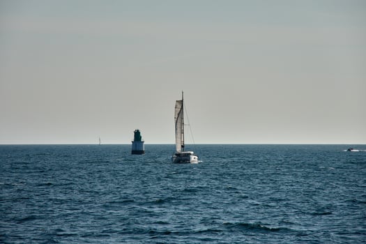 A sailing boat crossing the Vigo Estuary next to a lighthouse with the open sea and a clear sky on a peaceful sailing day photo