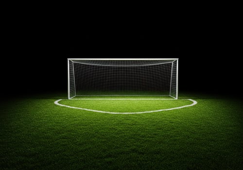 A soccer goal stands on a dark, grassy field with spotlight photo
