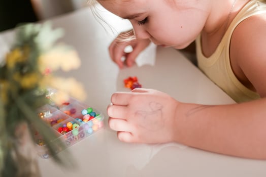 Little Girl is Concentrating on Crafting Colorful Jewelry with Beads at Home, Creative Activity. photo