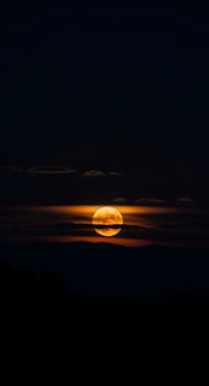 Ethereal glow of a full moon ascending over the horizon embraced by the clouds and watched from dark hills in the calm photo
