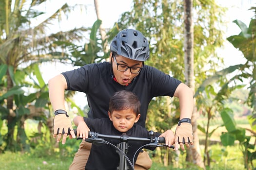 Happy Asian father and son riding bicycle together with park background photo