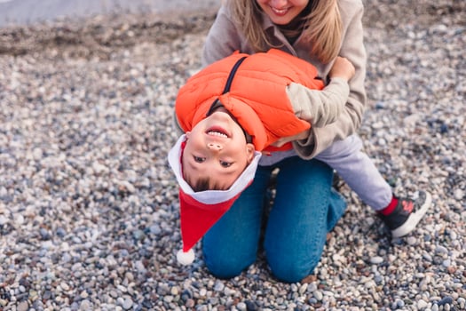 A mother and her young son play on a winter beach. The boy wears a Santa hat and an orange life jacket. They share joyful moments together. photo