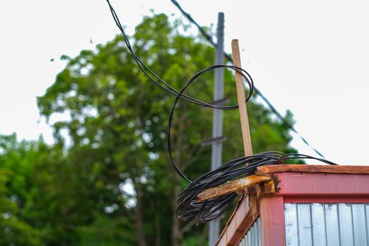Moscow, Russia, 18.06.2025 Coiled black electrical wires on rustic rusty container outdoors with green trees and electric pole in background. photo