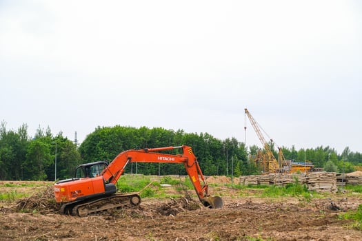 Moscow, Russia, 18.06.2025 An orange excavator at a construction site with a forest and cranes in the background. Construction machine for digging and earthmoving. photo