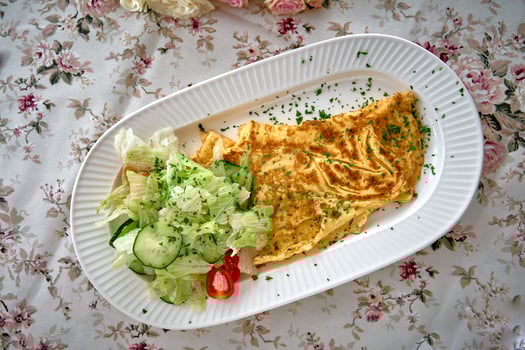 Deliciously Prepared Omelette Plated with Fresh Salad Garnished with Herbs on a Floral-Patterned Tablecloth Ideal for Breakfast or Brunch Lovers photo