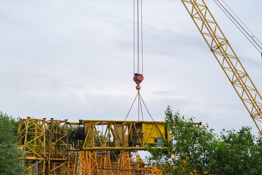 Moscow, Russia, 18.06.2025 Yellow construction tower crane hook lifting a large metal beam against a cloudy sky during the building process. Industrial work. photo
