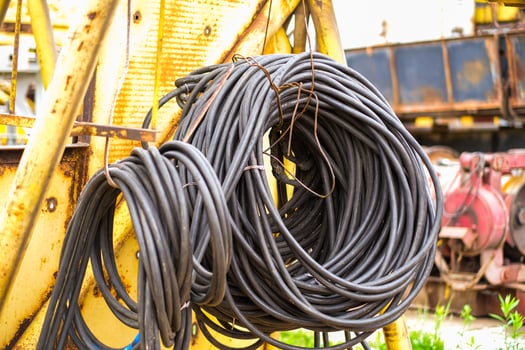 Moscow, Russia, 18.06.2025 Coiled black electrical cable hanging on a rusted yellow metal structure with industrial machinery in the background. Construction and power supply concept. photo