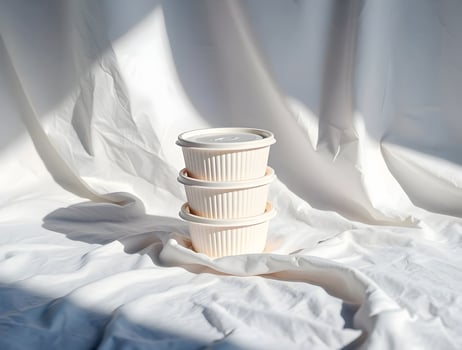 Three white containers sit on top of a white cloth photo