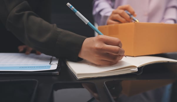 A man is writing on a piece of paper while another person is holding a pen photo