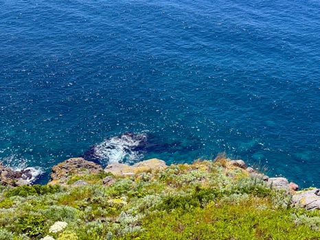 A peaceful ocean scene along rocky coastline, where waves gently crash against the shore. The lush green terrain blends into the blue sea, capturing the raw, natural spirit of frontier. photo
