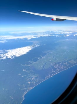 A high-altitude aerial view, showing a dramatic coastline, mountains and cities. Clouds drift above a vast natural landscape, captured through a plane window. Scenic or business flight travel photo. photo
