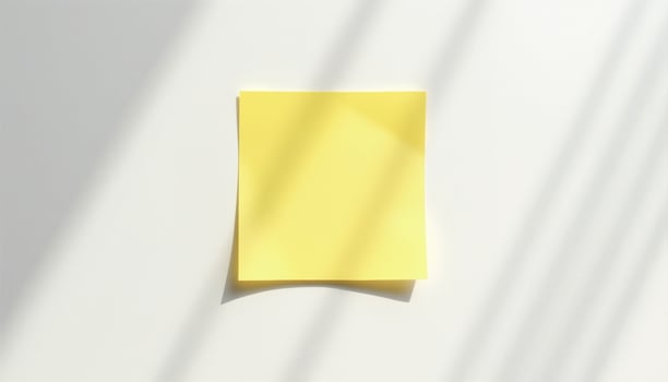 A blank yellow sticky note affixed to a white surface, casting subtle shadows. photo