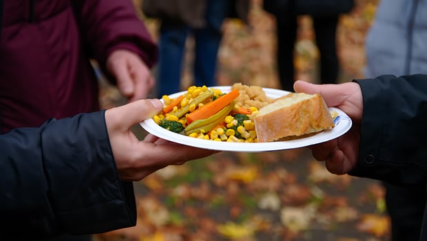 Hands Exchanging a Warm Plate of Mixed Vegetables and Bread at an Outdoor Autumn Gathering photo