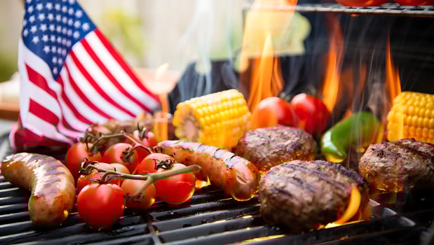Grilling burgers, sausages, corn, and tomatoes over hot flames with an American flag in the background. photo