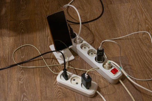 There are two dirty extension cords on the floor with various chargers and a phone connected to them photo