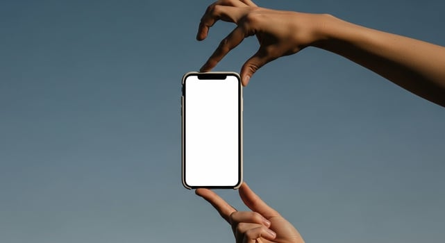 Hands holding a modern smartphone with a blank white screen against a clear blue sky photo