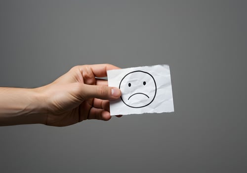 A person holding a piece of paper with a sad face drawn on it photo