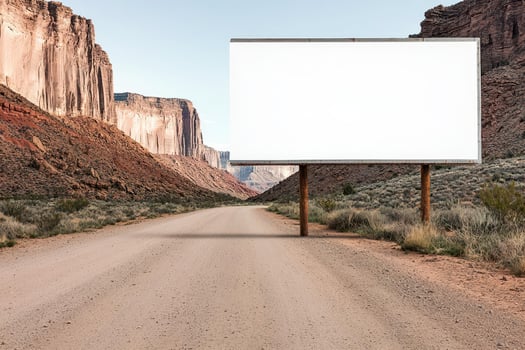 Blank billboard on a dirt road surrounded by rocky cliffs in a scenic landscape. photo