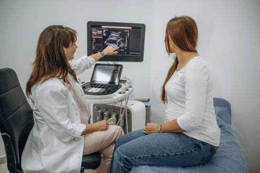 A woman is sitting in a chair while a doctor is looking at a monitor photo