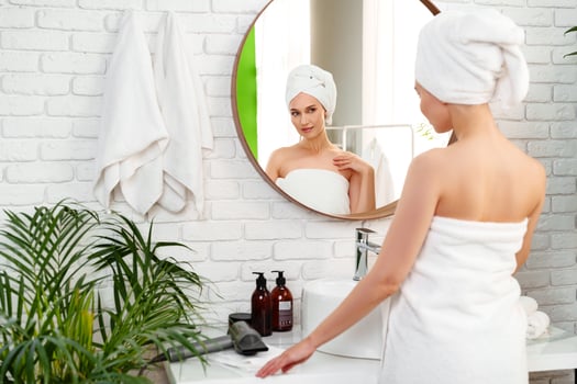 Woman preparing in a bright bathroom with a mirror and green plants after a relaxing shower photo
