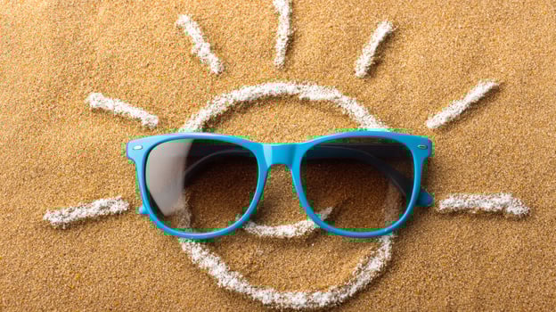 Vibrant sunglasses on sandy beach design. Bright blue sunglasses rest on warm sand with a sun shape drawn in the background, suggesting a sunny beach day. photo