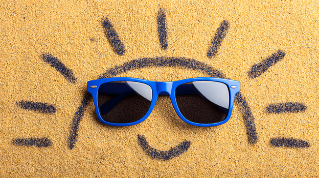 Sunglasses on sandy sun. Bright blue sunglasses are resting on golden sand with a cheerful sun design drawn in the background. photo