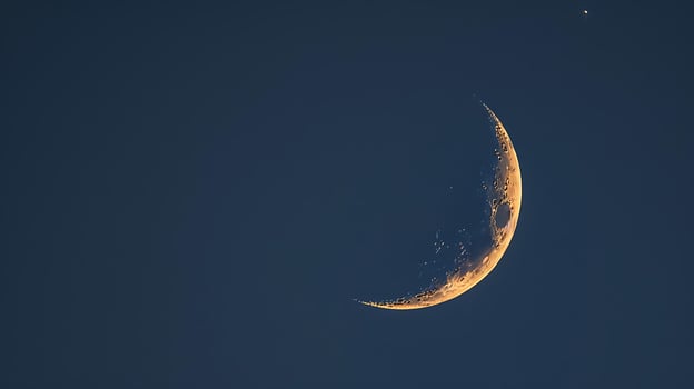 Crescent Moon Glows Orange Against Deep Blue Evening Sky. photo