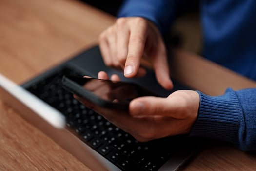 Person using smartphone while sitting at a desk in a cozy environment with a laptop nearby during daytime photo
