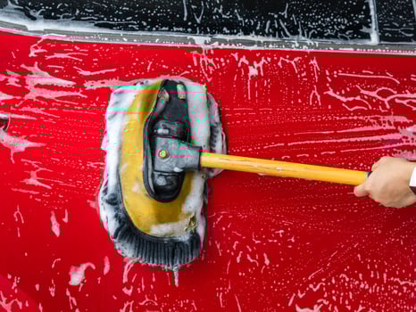 Close up of a person holding a mop washing a red car and cleaning it with foam at a self-service car wash. photo
