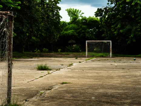 An empty outdoor soccer field with a goal with a net and an old soccer ball on the cement floor. Old sports equipment in a rural park. photo