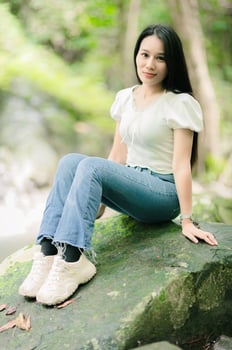 Serene Young Woman Sitting on a Rock by a Waterfall in Nature photo