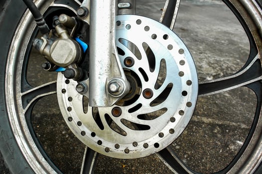Close-up of motorcycle front wheel with disc brake rotor and caliper on concrete background. photo