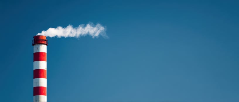 The striking red and white chimney releasing smoke into a clear blue sky. photo