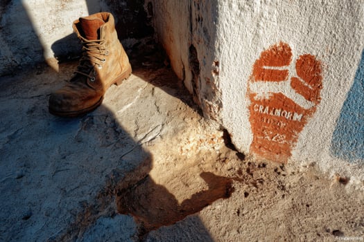 A boot and a shoe are on the ground next to a wall photo